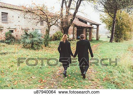 Picture - Rear view of couple strolling by old farm buildings. Fotosearch