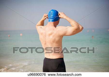 Stock Photograph - Rear view of mature man adjusting swimming cap on beach, Dubai, United Arab Emirates. Fotosearch