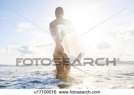 Rear view of woman carrying surfboard in sunlit sea, Nosara, Guanacaste Province, Costa Rica View Large Photo Image Stock Photograph - Rear view of woman carrying surfboard in sunlit sea, Nosara, Guanacaste Province, Costa Rica. Fotosearch