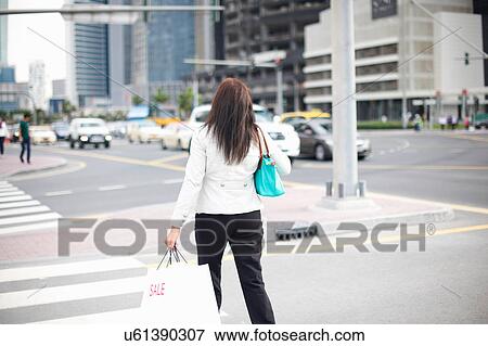 Stock Photo - Rear view of woman with shopping bags strolling along street, Dubai, United Arab Emirates. Fotosearch