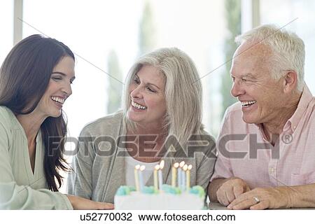 Stock Image - Senior couple and adult daughter with birthday cake. Fotosearch