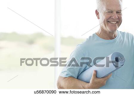 Stock Image - Senior man holding yoga mat. Fotosearch