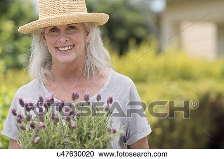 Stock Image - Senior woman holding pot plant. Fotosearch