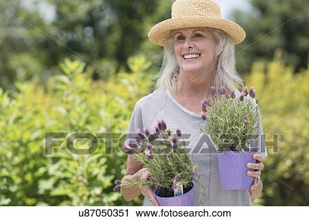 Stock Image - Senior woman holding pot plants. Fotosearch