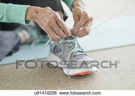 Stock Photograph - Senior woman lacing up trainers. Fotosearch
