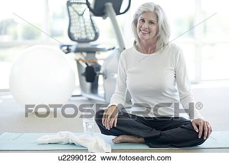 Stock Image - Senior woman sitting cross legged in gym. Fotosearch