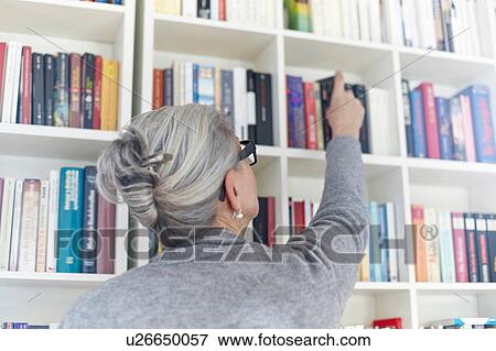 Stock Photo - Senior woman taking book from bookshelf, rear view. Fotosearch