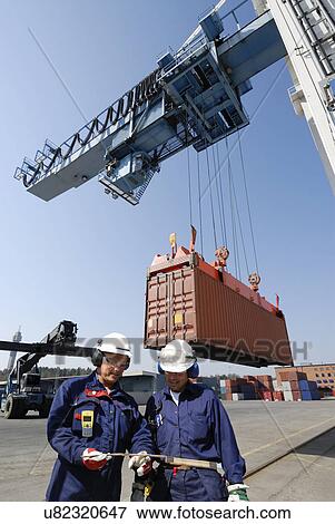 Stock Photo - Shipping workers with cargo container on crane. Fotosearch