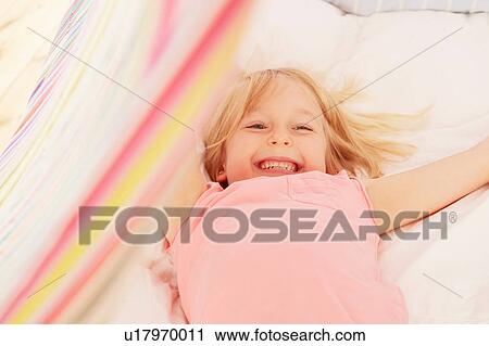 Stock Image - Smiling girl lying on back in tent. Fotosearch