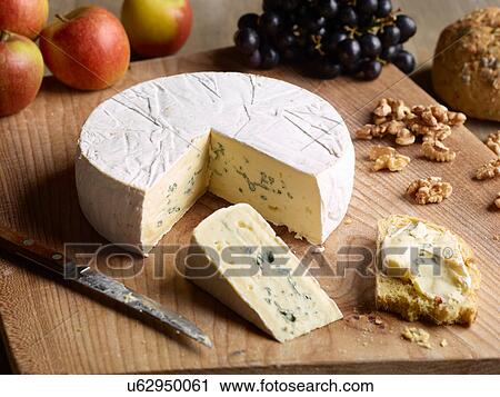 Stock Image - Still life of Blue brie with walnuts, grapes and apples on chopping board. Fotosearch