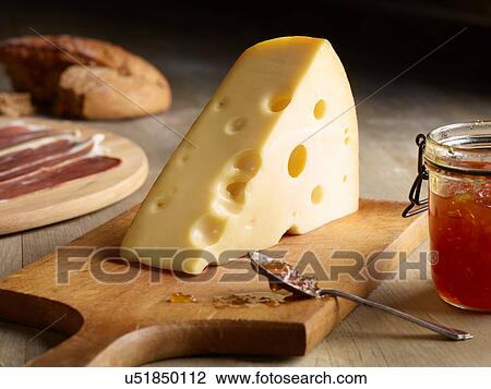 Stock Image - Still life of Edam cheese with quince chutney, on chopping board. Fotosearch