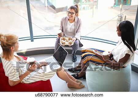 Stock Photo - Three businesswomen with takeaway coffee sitting on beanbags chatting. Fotosearch