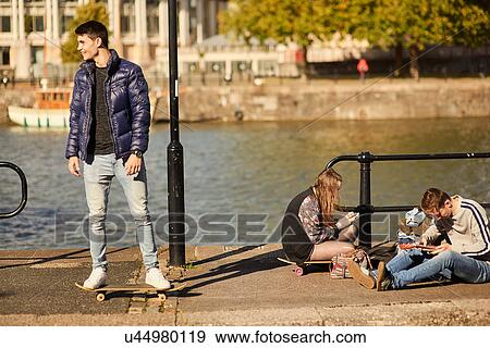 Stock Photo - Three friends fooling around beside river, young man on skateboard, Bristol, UK. Fotosearch