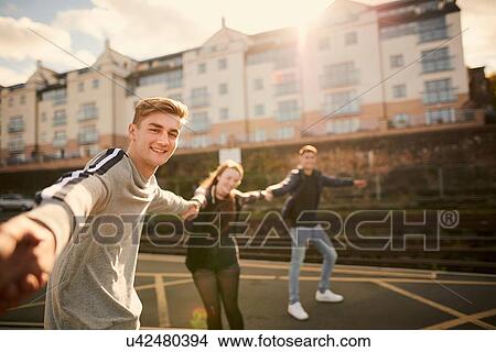 Picture - Three friends fooling around outdoors, holding hands, Bristol, UK. Fotosearch