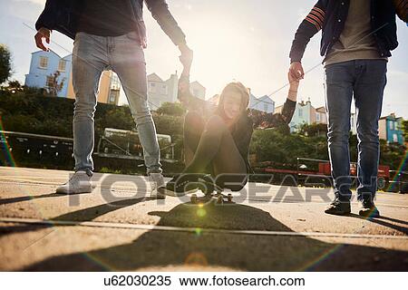 Stock Photography - Three friends fooling around outdoors, young men pulling young woman along on skateboard, Bristol, UK. Fotosearch