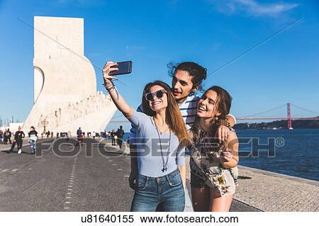 Stock Photography - Three friends, outdoors, taking selfie with smartphone, Monument to the Discoveries in background, Lisbon, Portugal. Fotosearch