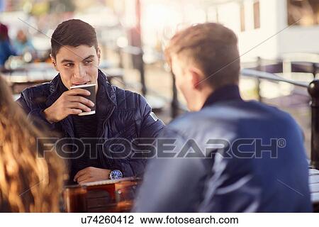 Stock Image - Three friends sitting outdoors, drinking coffee, Bristol, UK. Fotosearch