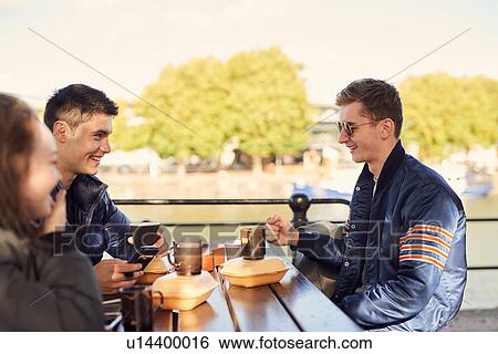 Stock Photograph - Three friends, sitting outdoors, drinking hot drinks, Bristol, UK. Fotosearch