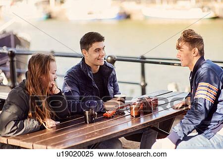 Stock Photography - Three friends sitting outdoors, drinking hot drinks, Bristol, UK. Fotosearch