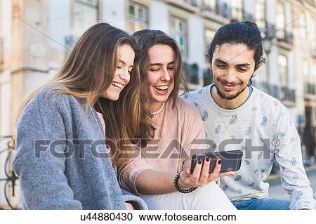Stock Image - Three friends sitting outdoors, taking selfie with smartphone, Lisbon, Portugal. Fotosearch
