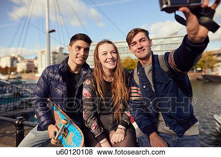 Three friends sitting outdoors, taking selfie with camera, Bristol, UK View Large Photo Image Stock Photo - Three friends sitting outdoors, taking selfie with camera, Bristol, UK. Fotosearch