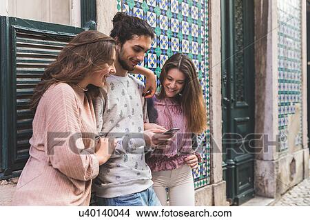 Picture - Three friends, standing in street, looking at smartphone, Lisbon, Portugal. Fotosearch