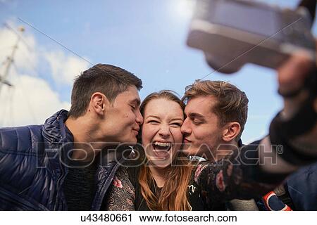 Three friends taking selfie with camera, young men kissing young woman on cheek, Bristol, UK View Large Photo Image Stock Image - Three friends taking selfie with camera, young men kissing young woman on cheek, Bristol, UK. Fotosearch