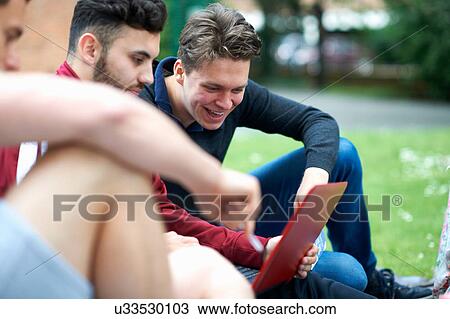 Stock Image - Three male friends, sitting outdoors, looking at digital tablet. Fotosearch
