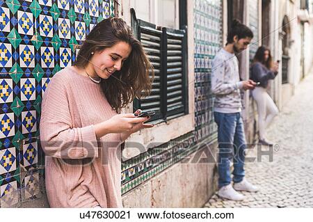 Three young adults standing in street, looking at their own smartphones, Lisbon, Portugal View Large Photo Image Stock Image - Three young adults standing in street, looking at their own smartphones, Lisbon, Portugal. Fotosearch