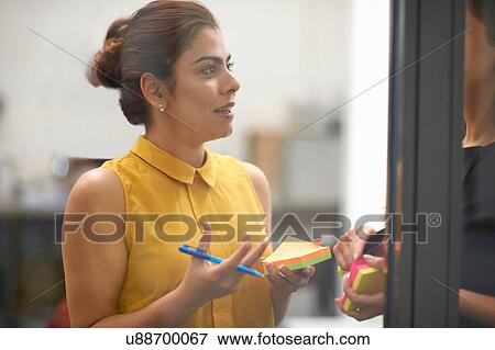 Stock Photo - Two businesswomen behind office glass wall having discussion. Fotosearch