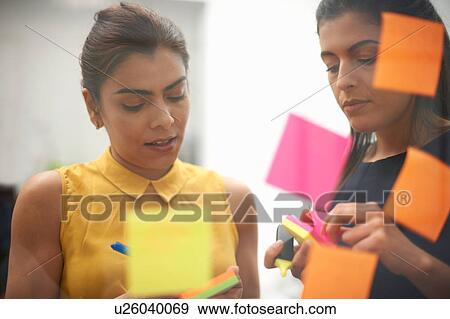Stock Photo - Two businesswomen writing on sticky notes for office glass wall. Fotosearch