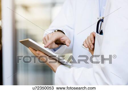 Stock Image - Two doctors looking at digital tablet, mid section, close-up. Fotosearch