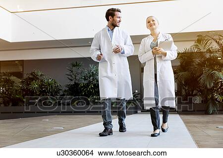 Two doctors walking, female doctor holding digital tablet View Large Photo Image Picture - Two doctors walking, female doctor holding digital tablet. Fotosearch