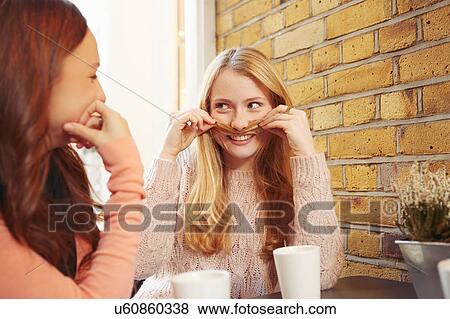 Two female friends, sitting outdoors, having coffee, fooling around View Large Photo Image Stock Photo - Two female friends, sitting outdoors, having coffee, fooling around. Fotosearch