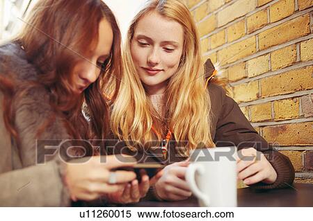 Two female friends, sitting outdoors, having coffee, looking at smartphone View Large Photo Image Stock Photography - Two female friends, sitting outdoors, having coffee, looking at smartphone. Fotosearch
