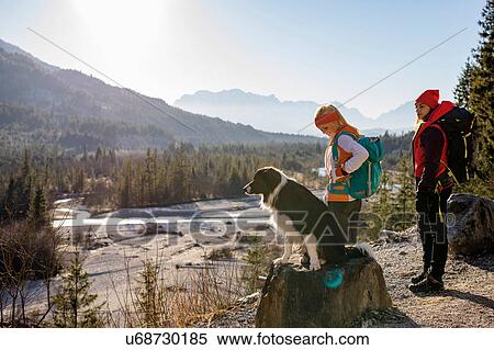 Stock Photography - Two female hikers and dog looking out over valley in Bavarian Alps. Fotosearch