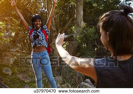 Stock Image - Two friends hiking, young woman taking photograph of friend, using smartphone, Cape Town, South Africa. Fotosearch