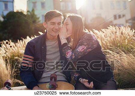Two friends sitting outdoors, young woman whispering to young man, Bristol, UK View Large Photo Image Stock Photography - Two friends sitting outdoors, young woman whispering to young man, Bristol, UK. Fotosearch
