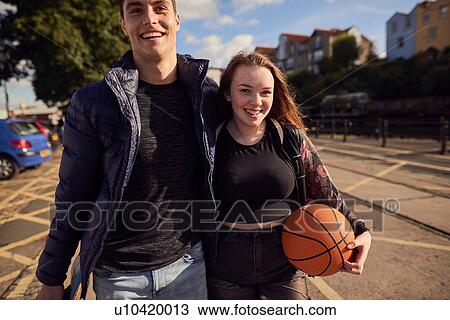 Stock Image - Two friends walking outdoors, young woman holding basketball, Bristol, UK. Fotosearch