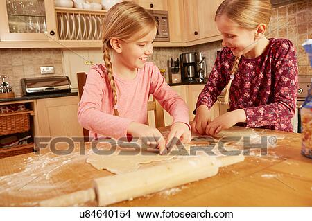 Picture - Two girls baking together at kitchen table. Fotosearch