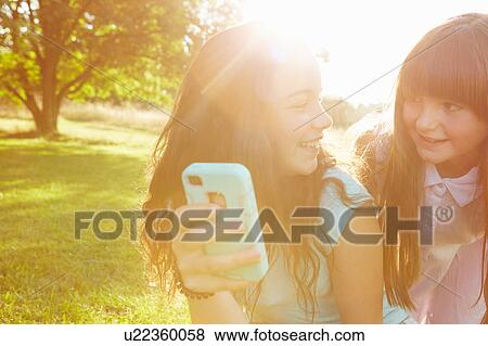Two girls looking at smartphone in sunlit park View Large Photo Image Stock Photo - Two girls looking at smartphone in sunlit park. Fotosearch