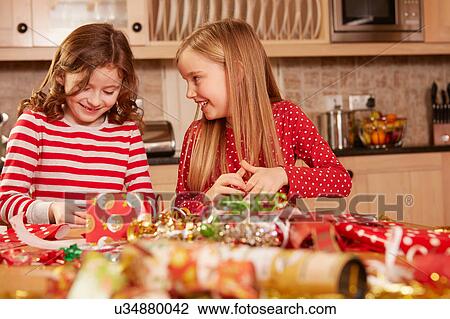 Stock Image - Two girls wrapping christmas presents at table. Fotosearch