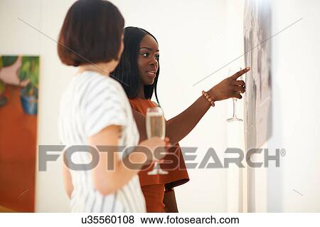 Two women pointing at oil paintings at art gallery opening View Large Photo Image Stock Photo - Two women pointing at oil paintings at art gallery opening. Fotosearch