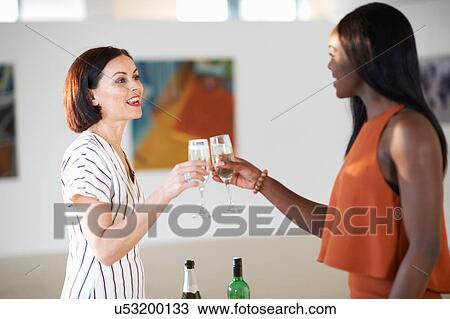 Stock Image - Two women raising a white wine toast at art gallery opening. Fotosearch