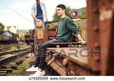 Two young men by train track, carrying skateboard, Bristol, UK View Large Photo Image Stock Photo - Two young men by train track, carrying skateboard, Bristol, UK. Fotosearch
