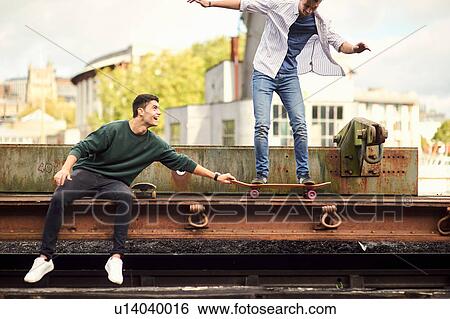Two young men fooling around by train track, balancing on skateboard Bristol, UK View Large Photo Image Stock Photograph - Two young men fooling around by train track, balancing on skateboard Bristol, UK. Fotosearch