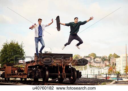 Stock Image - Two young men jumping from trailer on train track, Bristol, UK. Fotosearch