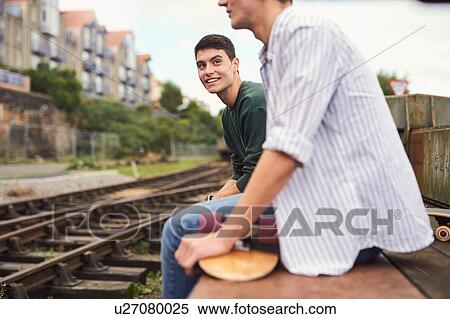Two young men sitting by train track, Bristol, UK View Large Photo Image Stock Photography - Two young men sitting by train track, Bristol, UK. Fotosearch