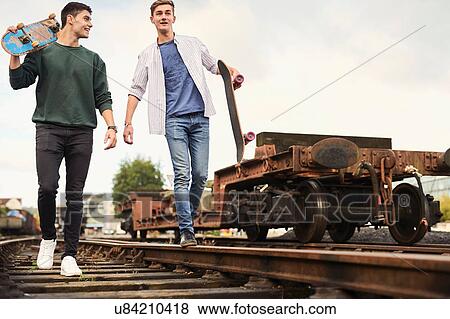 Two young men walking along train track, carrying skateboards, Bristol, UK View Large Photo Image Stock Photo - Two young men walking along train track, carrying skateboards, Bristol, UK. Fotosearch