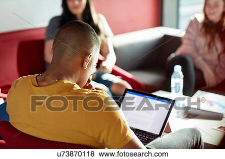 Stock Photo - University student using laptop, relaxing with student friends. Fotosearch